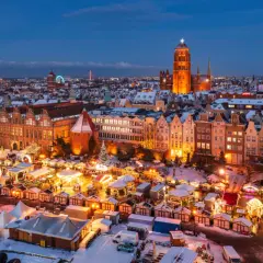 Gdańsk jarmark świąteczny nocą, z oświetlonymi kramami, karuzelą i zabytkową zabudową w tle.