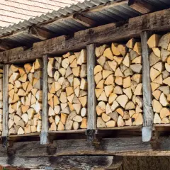 Stosy drewna opałowego, starannie ułożone w drewnianej szopie, czekają na suszenie.