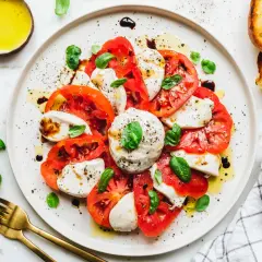 Caprese-Salat mit frischen Tomaten, veganem Mozzarella und Basilikum, beträufelt mit Olivenöl und Balsamico. Dazu geröstetes Brot.
