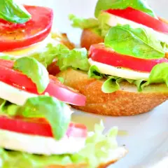 Mini kanapki z mozzarellą, pomidorem, sałatą i bazylią na chrupiącej bagietce.