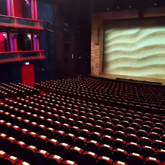 Puste rzędy czerwonych foteli w teatrze, z widownią i sceną z piaskowym tłem. Gdzie jest teatr Roma?