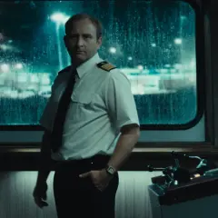 Kapitan w białej koszuli i krawacie stoi przy sterach statku. Scena z jednego z filmów Jana Holoubka.