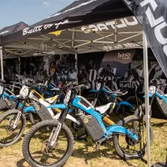 Varias motocicletas Bultaco Brinco eléctricas, de colores azul y blanco, expuestas bajo una carpa.