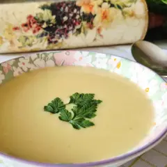 Aksamitna zupa z białych szparagów, udekorowana natką pietruszki, czeka na łyżkę. Obok leży ozdobiony wałek do ciasta.