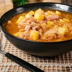 Parzybroda, sycąca zupa z kapusty kiszonej, ziemniaków i mięsa, podana w czarnej misce, obok leży łyżka.