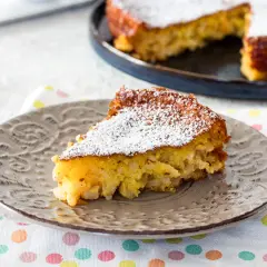 Una fetta di torta di riso, la ricetta della nonna, cosparsa di zucchero a velo su un piatto grigio.