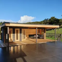 Modern cabin with porches cerrados de obra, deck, and outdoor seating, set against a green hillside with sheep.