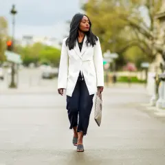 Mujer con abrigo blanco y vaqueros oscuros, luciendo un *dress code smart* mientras camina por la calle.