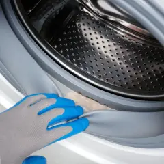 Hand in blue glove cleans the washing machine door seal. A clean ablaufschlauch waschmaschine reinigen is important for hygiene.