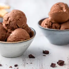 Due ciotole piene di cremoso gelato al cioccolato, con pezzi di cioccolato sparsi sul tavolo.