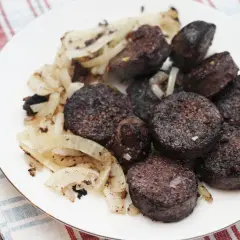 Kaszanka pokrojona w plastry z podsmażoną cebulą na białym talerzu.
