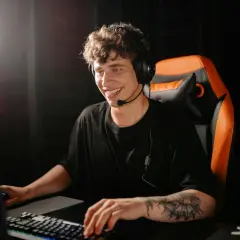 Uśmiechnięty gracz w słuchawkach siedzi przy komputerze, gotowy do gry. Jeśli zapomniałeś hasła, dowiedz się, jak zresetować hasło na Steam.