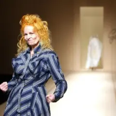 Vivienne Westwood, con su icónico cabello naranja, posa con energía en la pasarela de Westwood, luciendo un vestido a rayas azules y grises.