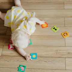 Dziecko z jasnymi włosami leży na podłodze, bawiąc się puzzlami. To etap rozwoju, kiedy dziecko powinno się obracać.