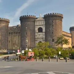 Castel Nuovo w Neapolu, imponująca forteca z wieżami i bramą, to jedno z miejsc, które warto zobaczyć. Obok przejeżdża dorożka.
