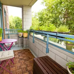 Zielony balkon z meblami i roślinami. Jak osłonić balkon w bloku? Rośliny na balustradzie i drewniana podłoga dodają uroku.