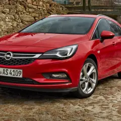 Czerwony Opel Astra Sports Tourer zaparkowany na kamienistej nawierzchni, z kamiennym murem w tle.