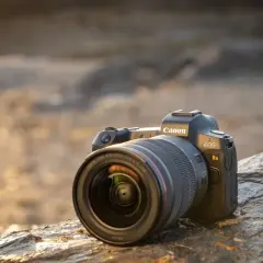 Profesjonalny aparat do astrofotografii Canon EOS Ra z obiektywem RF 15-35mm f/2.8 L IS USM leży na kamieniu.