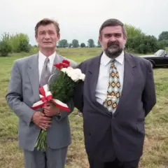 Wspólnik kilera z komedii Machulskiego, z bukietem kwiatów, obok kolegi i czarnego kabrioletu na łące.
