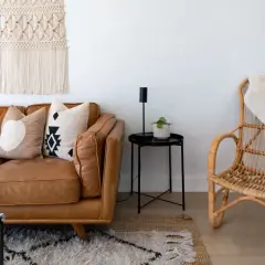 A cozy living room with a brown leather sofa, patterned pillows, a macrame wall hanging, and a rattan chair, embodying a relaxed bohemian furniture style.