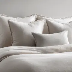 A bed with a duvet and several pillows, including what is a standard sham, all in neutral tones.