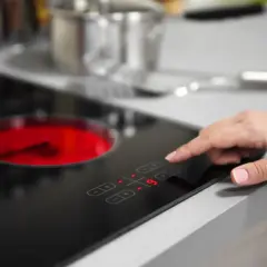 Dłoń dotyka panelu sterowania, wybierając moc na płycie elektrycznej, która może być też indukcyjną.