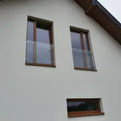 Nowoczesny portfenetr z drewnianymi ramami i szklaną balustradą na białej elewacji.