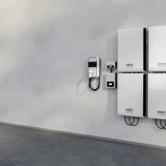Cztery białe moduły magazynowania energii "ENERGY STORAGE" zamontowane na szarej ścianie obok ładowarki EV.