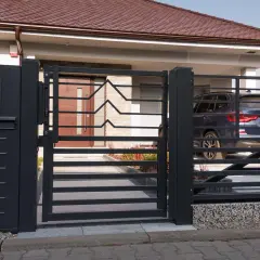 Nowoczesne, ciemnoszare ogrodzenie z furtką i domofonem prowadzi do wejścia do domu. Za bramą stoi ciemny SUV.