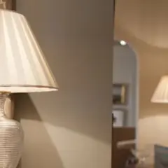Lámpara de mesa con pantalla blanca a rayas, reflejada en un espejo junto a otra lámpara.