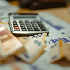Rechner und Euro-Scheine liegen auf einem Finanzbericht. Eine Witwe überlegt ihre Steuerklasse.