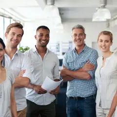 A diverse team smiles confidently, showcasing what employee engagement looks like. They stand together in a bright office, radiating positivity and collaboration.
