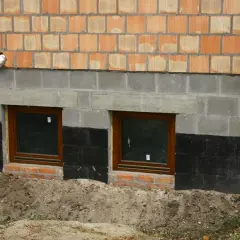 Wzmocnienie fundamentów w starym domu: nowe okna piwniczne, izolacja i warstwa cegieł.