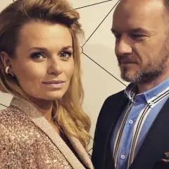 Emilia Komarnicka z pierwszym mężem, w eleganckich strojach, pozują do zdjęcia na tle geometrycznej ściany.