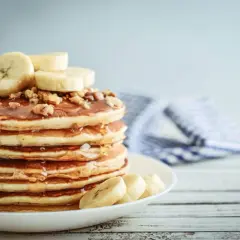 Una pila de tortitas de plátano cubiertas de miel y nueces, con rodajas de plátano fresco encima.