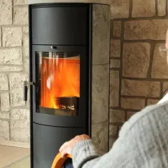 Älterer Mann sitzt vor einem brennenden Kaminofen. Die Idee, den Kamin stilllegen, kommt auf, wenn man ihn nicht mehr braucht.