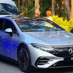 Srebrny Mercedes EQS z niebieskim podświetleniem prezentuje się efektownie na tle zieleni.