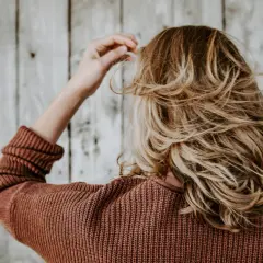 Kvinna med blont, vågigt hår som rör vid det. Kanske hon undrar hur får man tjockare hår?