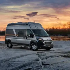 Srebrny kamper Globe-Traveller na tle zachodzącego słońca nad rzeką. Idealny, jaki kamper dla 2 osób na zimową podróż.