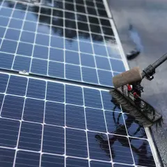 Brosse rotative en action pour nettoyer panneau solaire. L'eau ruisselle sur les cellules bleues et brillantes.