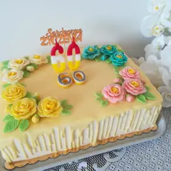 Żółty tort z ozdobami kwiatowymi i świeczkami w kształcie cyfr 60.