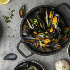 Una deliciosa preparación de mejillones, mostrando que son los mejillones, servidos en una sartén negra con perejil fresco y limón.