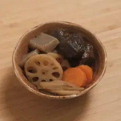A bowl of simmered vegetables, including shiitake mushrooms, lotus root, carrots, and konjac, likely part of a mushroom dashi broth.
