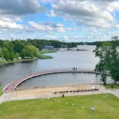 Malownicze jezioro w Szczecinku z łukowatym mostkiem, piaszczystą plażą i zielonymi terenami rekreacyjnymi.