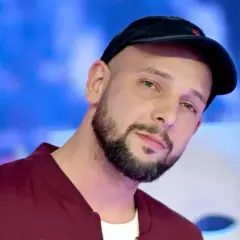 Maciej Pela, znany z ekranu, w czapce i kamizelce. Jego życiorys to historia sukcesu.