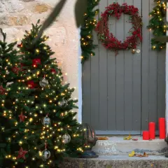 Árbol de Navidad iluminado y una corona de acebo adornan la entrada de una casa de piedra.