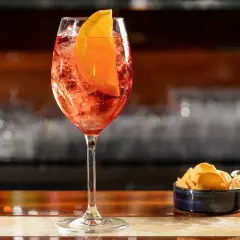 Un bicchiere di Spritz con fetta d'arancia, ghiaccio e stuzzichini. La spritz ricetta perfetta per l'aperitivo.