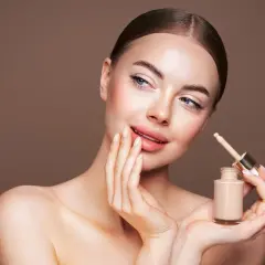 Kobieta z gładką cerą trzyma buteleczkę podkładu z pipetką.