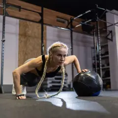 Kobieta wykonuje pompki z piłką lekarską, ćwicząc siłę i wytrzymałość. To świetny sposób, jak trenować crossfit.