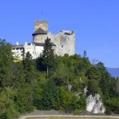 Zamek w Niedzicy, majestatyczna twierdza na wzgórzu, otoczona zielenią, z widokiem na jezioro i góry.